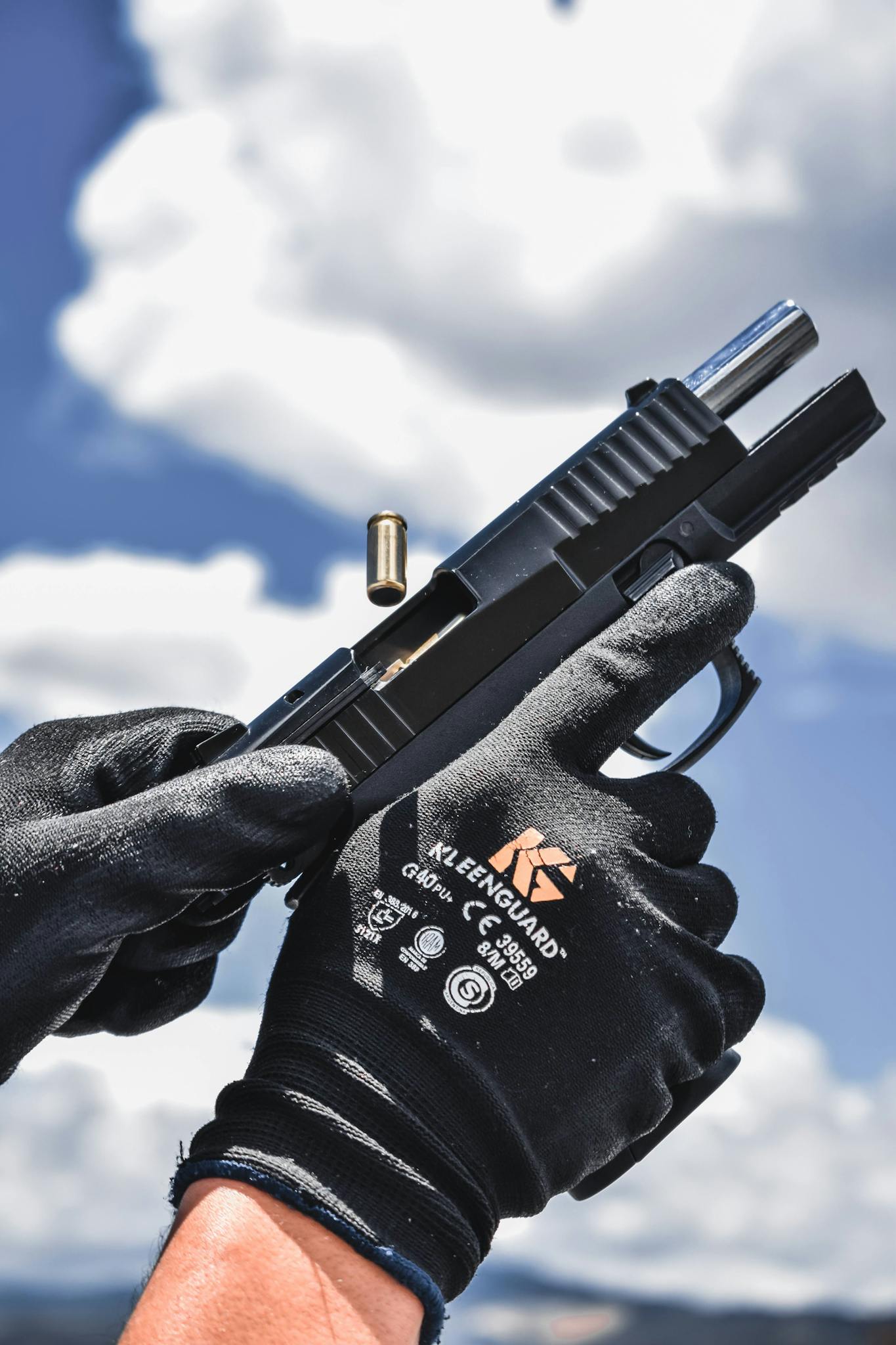 Detailed image of gloved hands reloading a pistol against a bright sky background.